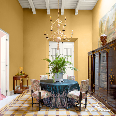 Bright yellow dining room with white beamed ceiling, teal tablecloth, fabric chairs, large cabinet